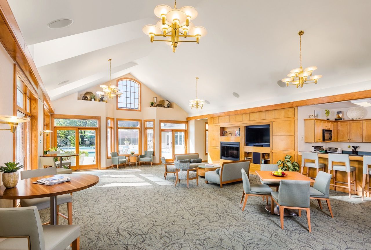 Bright resident lounge with vaulted ceiling, large windows, and multiple seating areas.
