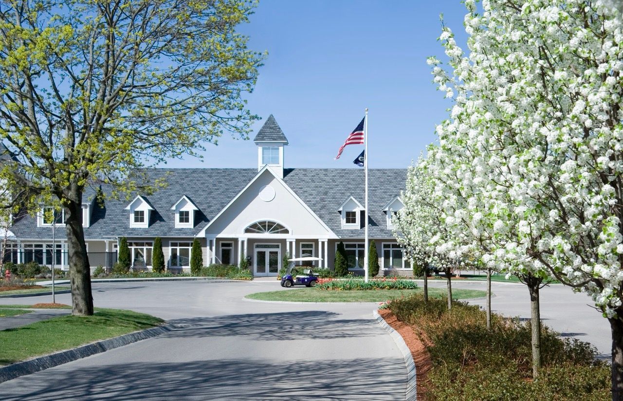 Exterior view of apartment community with front entrance, flagpole, and landscaped circle drive.