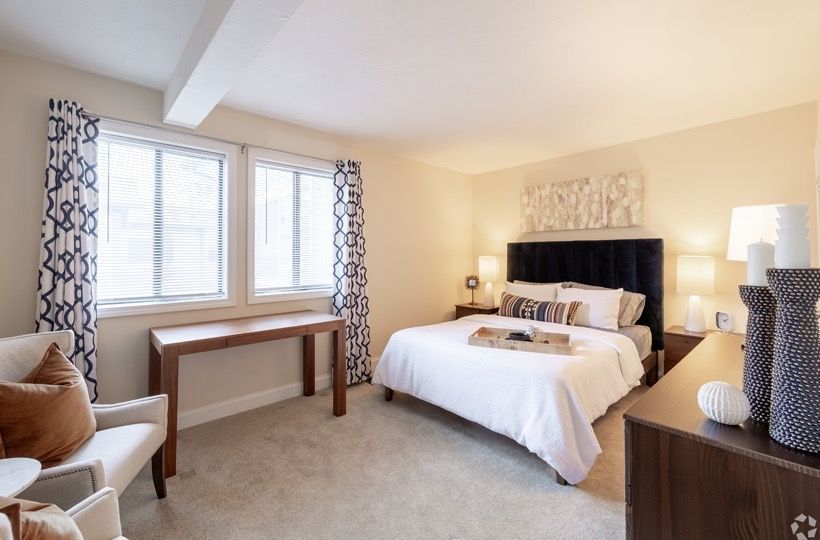 Bedroom in an apartment with a king bed, two windows, a desk, and seating area.