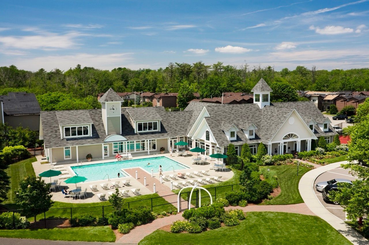 Aerial view of a resort-style pool and clubhouse at a green multifamily community.