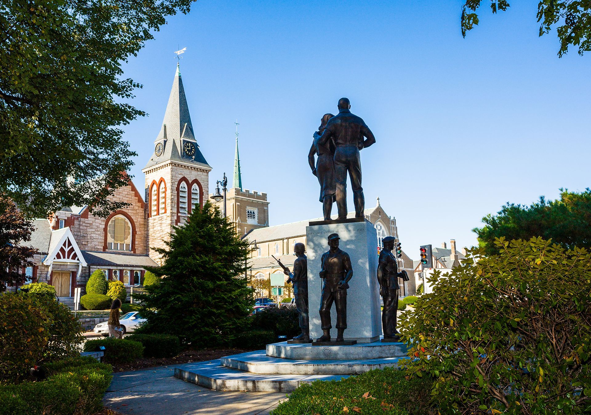 Bronze statue in a park with a church and trees under a blue sky