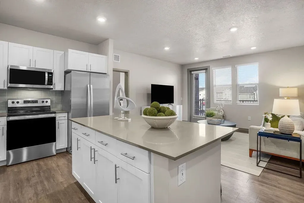 Modern kitchen with stainless steel appliances and an island, adjacent to a living area with a sofa and television at Valley View, offering apartments in Magna, UT.
