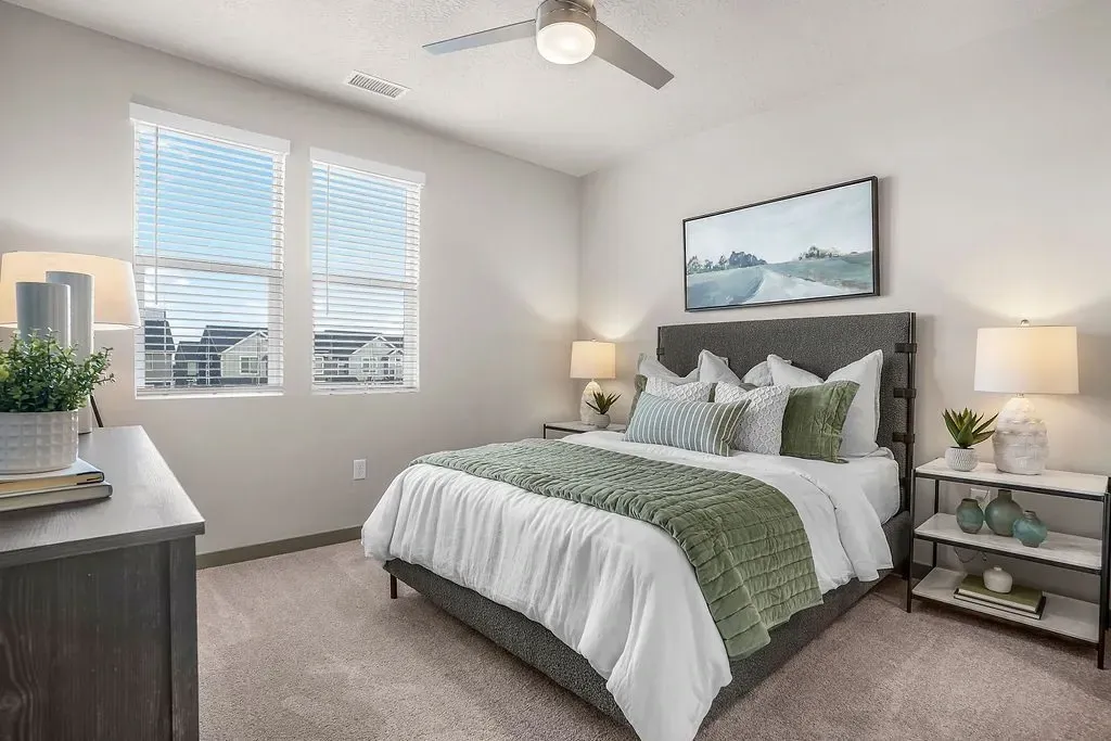 Cozy bedroom with a queen-size bed, plush green bedding, and two windows overlooking the neighborhood at Valley View, offering apartments in Magna, UT.