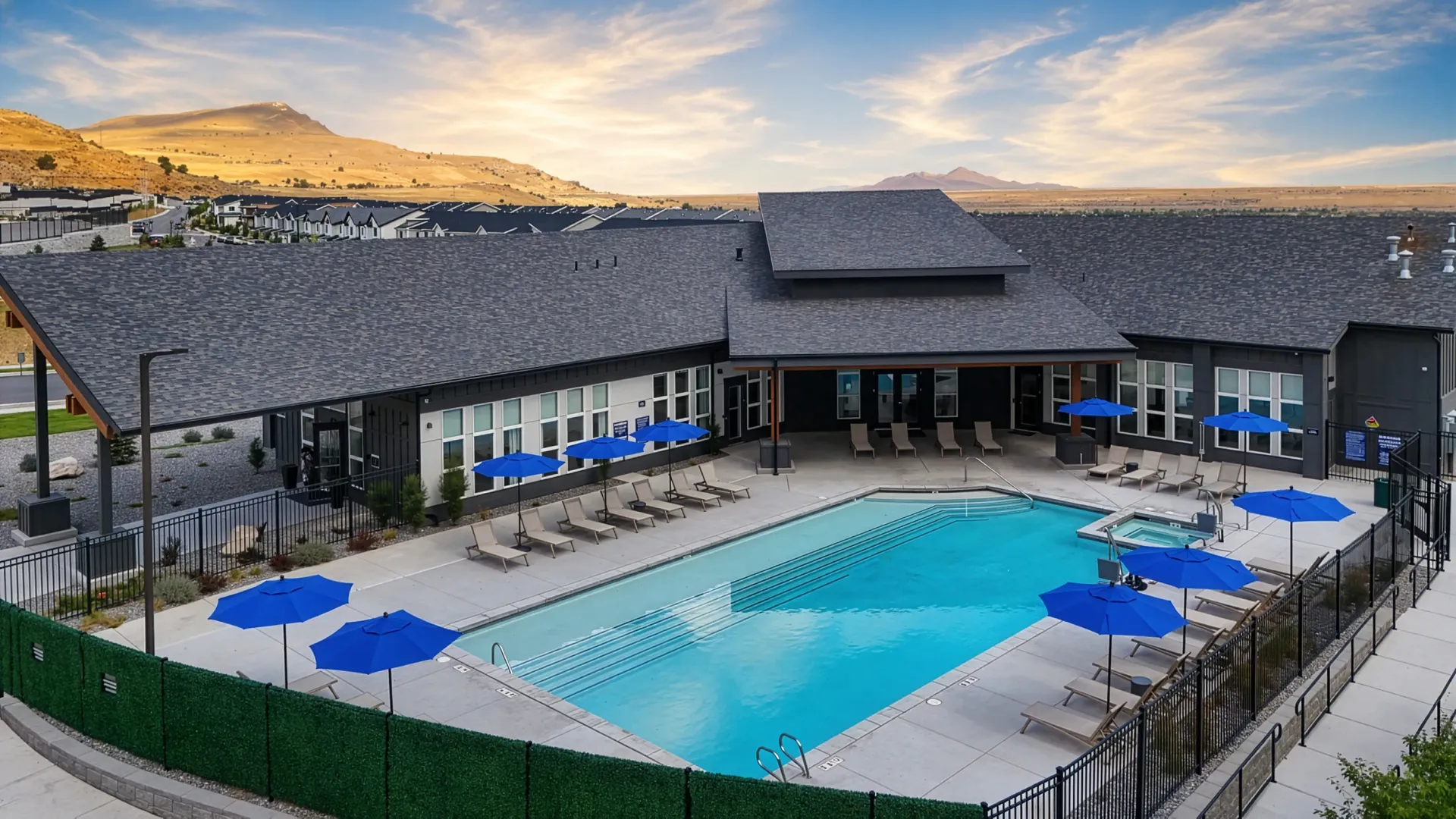 Swimming pool and hot tub area with lounge chairs and blue umbrellas, overlooking distant mountains at Valley View, offering apartments in Magna, UT.
