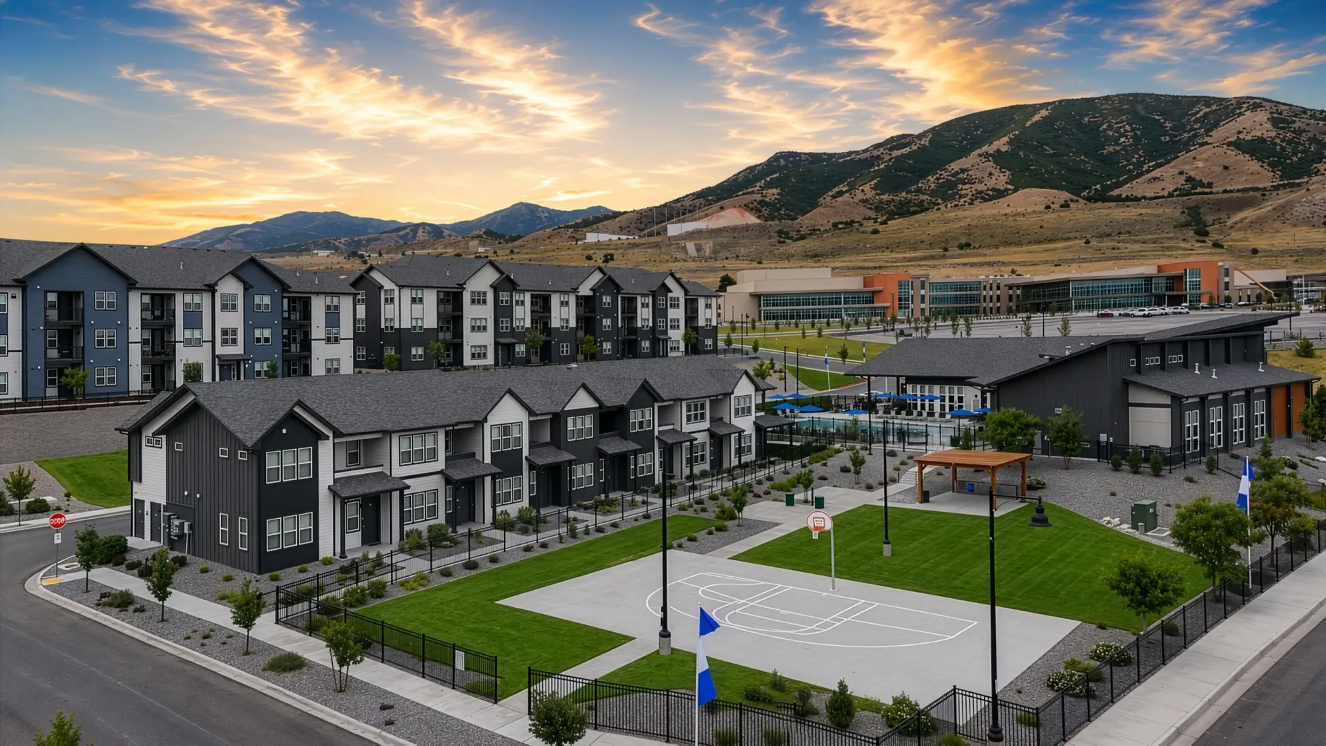 Exterior view of a modern apartment complex with townhomes and apartment buildings, a pool, and a basketball court at sunset at Valley View, offering apartments in Magna, UT.