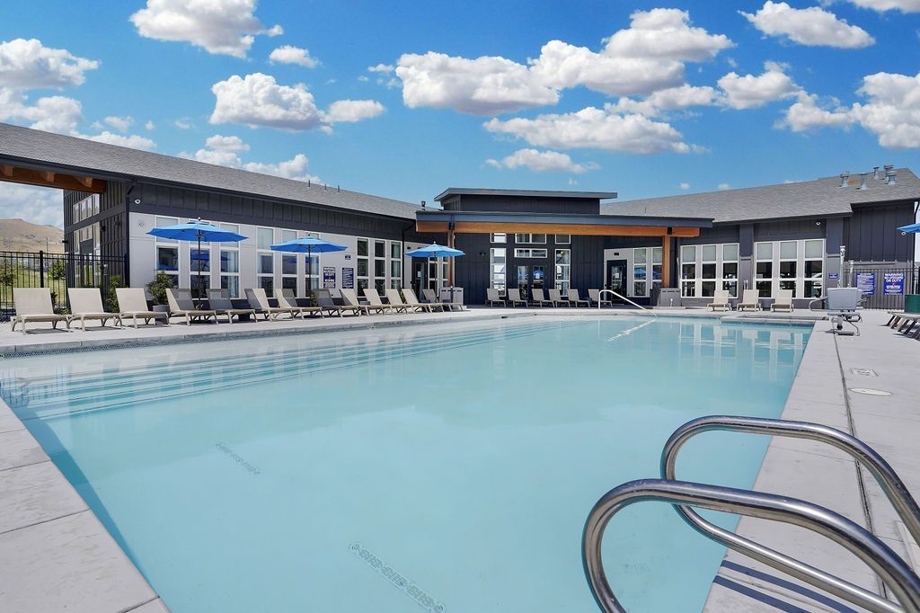 Outdoor pool at modern apartment community with lounge chairs and blue umbrellas at Valley View, offering townhomes for rent in Magna, UT.