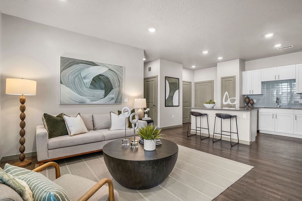 Open-concept living room and kitchen in a modern apartment, featuring a gray sofa, round coffee table, and bar stools at Valley View, offering pet-friendly apartments in Magna, UT.