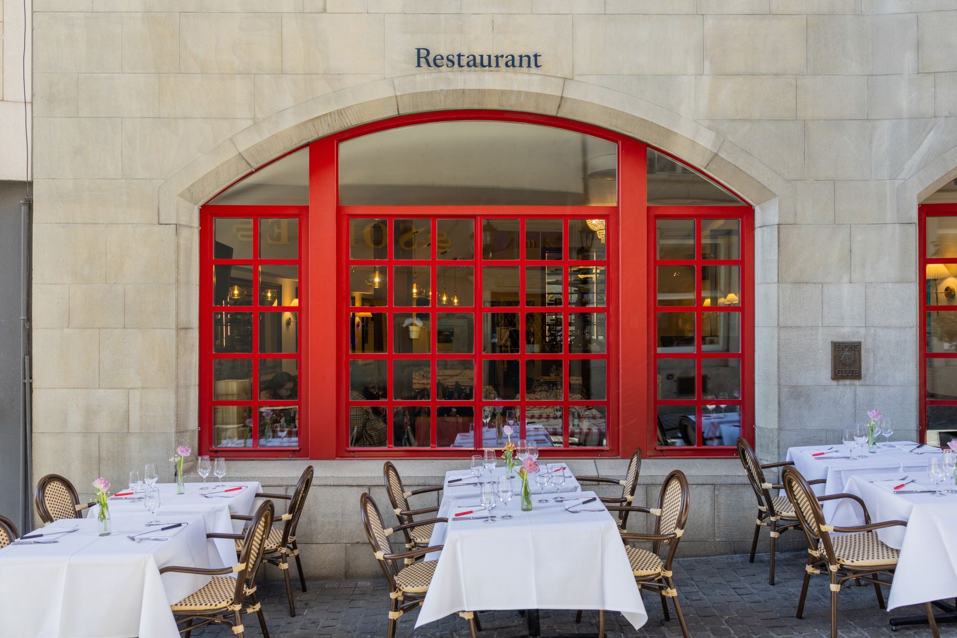 Narrow cobblestone alley with café tables and red storefronts under old European buildings