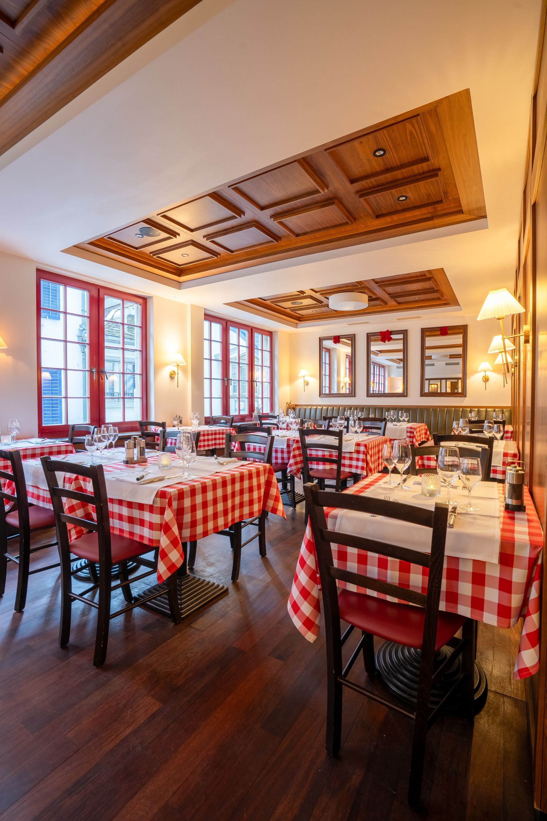 Leerer Speisesaal eines Restaurants mit rot-weiß karierten Tischdecken und großen Fenstern