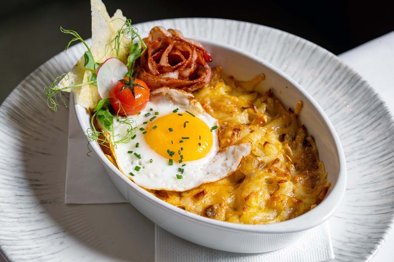 Gebackener Eier-Käse-Auflauf in einer weißen ovalen Form, garniert mit Kräutern und knusprigen Zwiebeln
