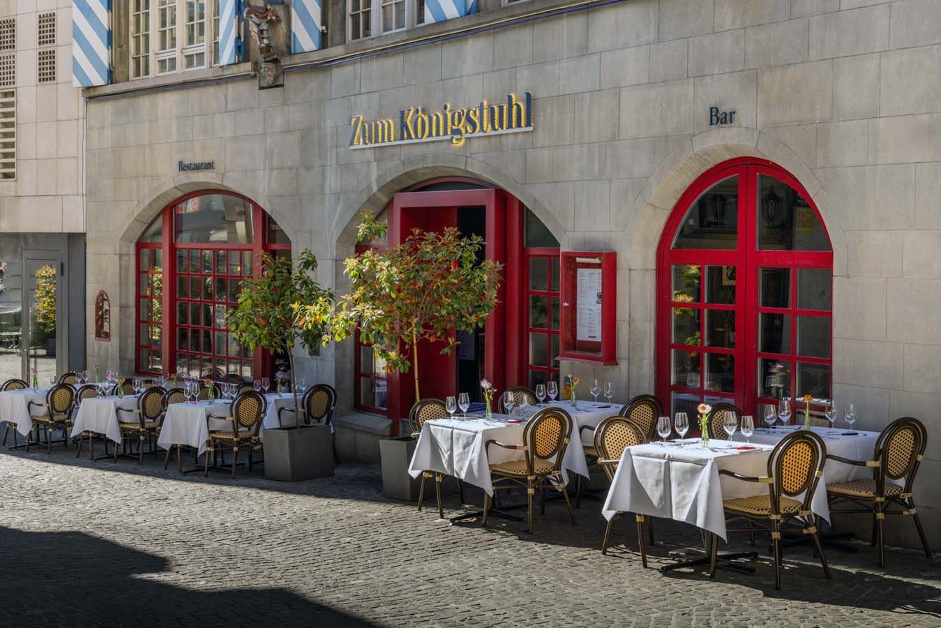 Entrance to Zum Königspalast restaurant with red doors and windows on a stone facade