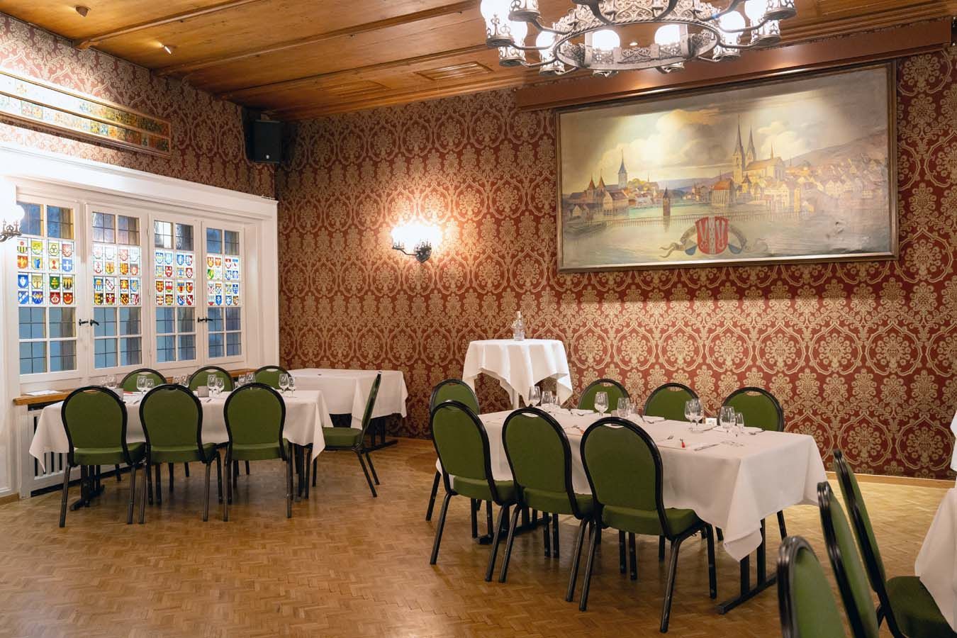 Elegantes Esszimmer mit gedeckten Tischen, grünen Stühlen, gemusterter Tapete und einem großen Wandgemälde