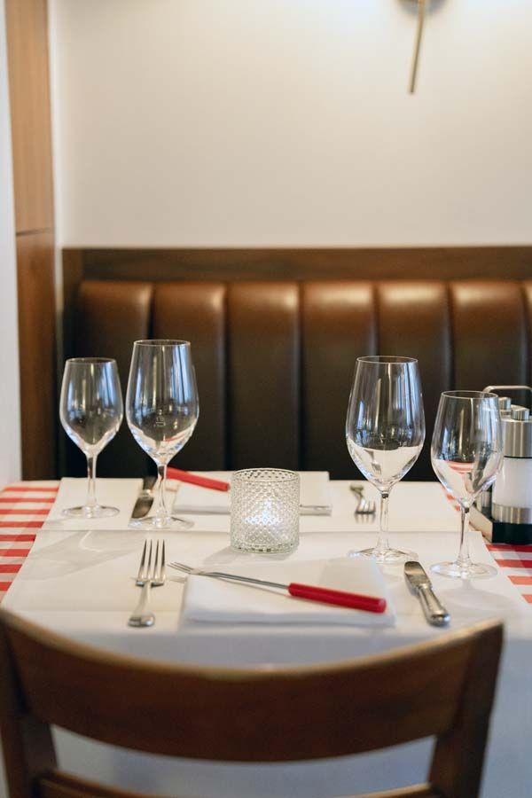 Decken Sie den Restauranttisch mit rot-weiß karierter Tischdecke, Weingläsern, Tellern und Besteck an einer Ledersitzbank.