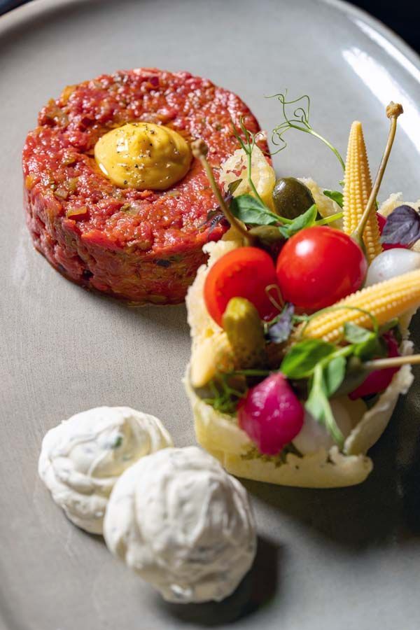 Gourmet-Vorspeise mit Tatar, Gemüse und cremigen Garnierungen auf einem grauen Teller