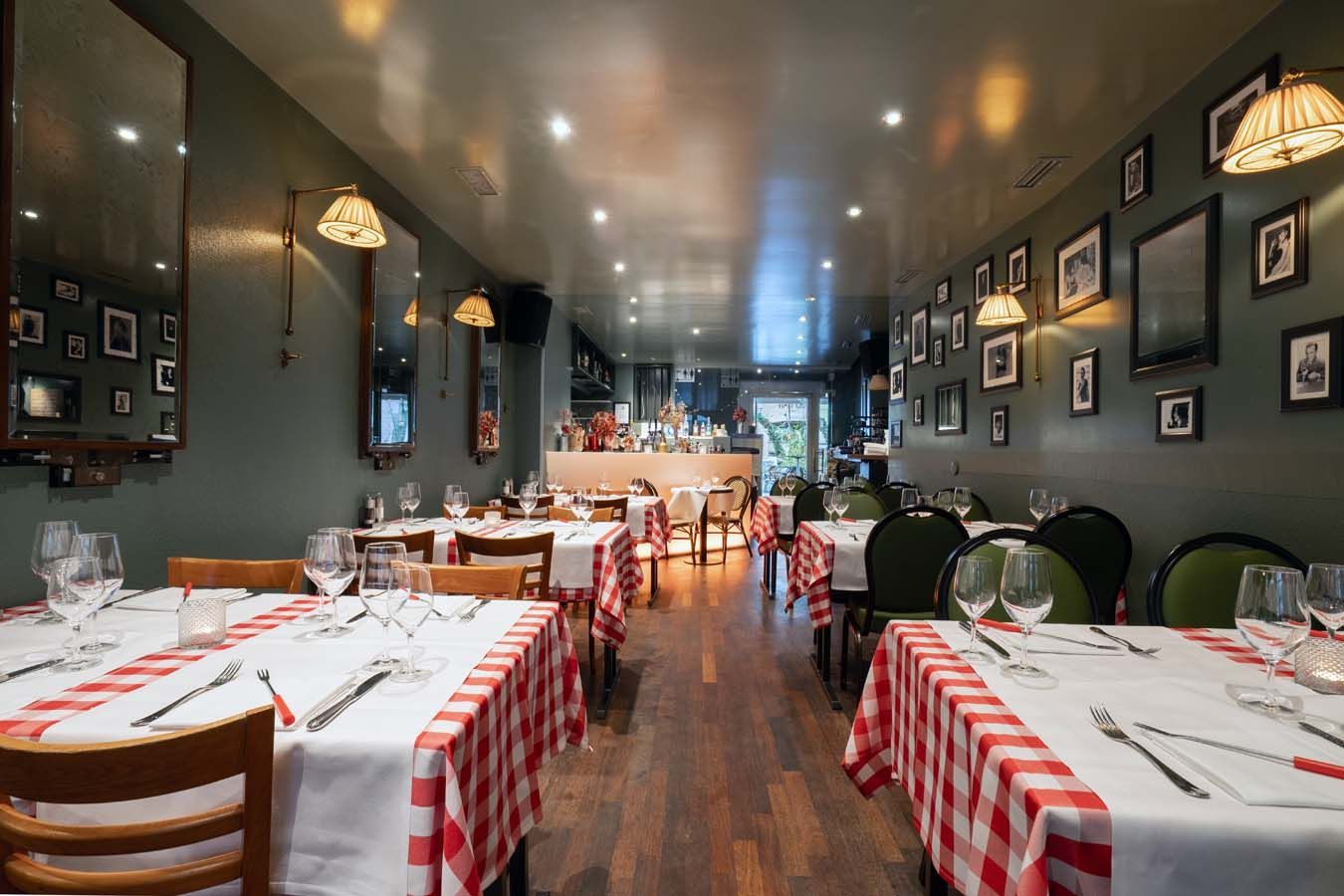 Leerer Speisesaal eines Restaurants mit rot-weiß karierten Tischdecken und Wandfotos