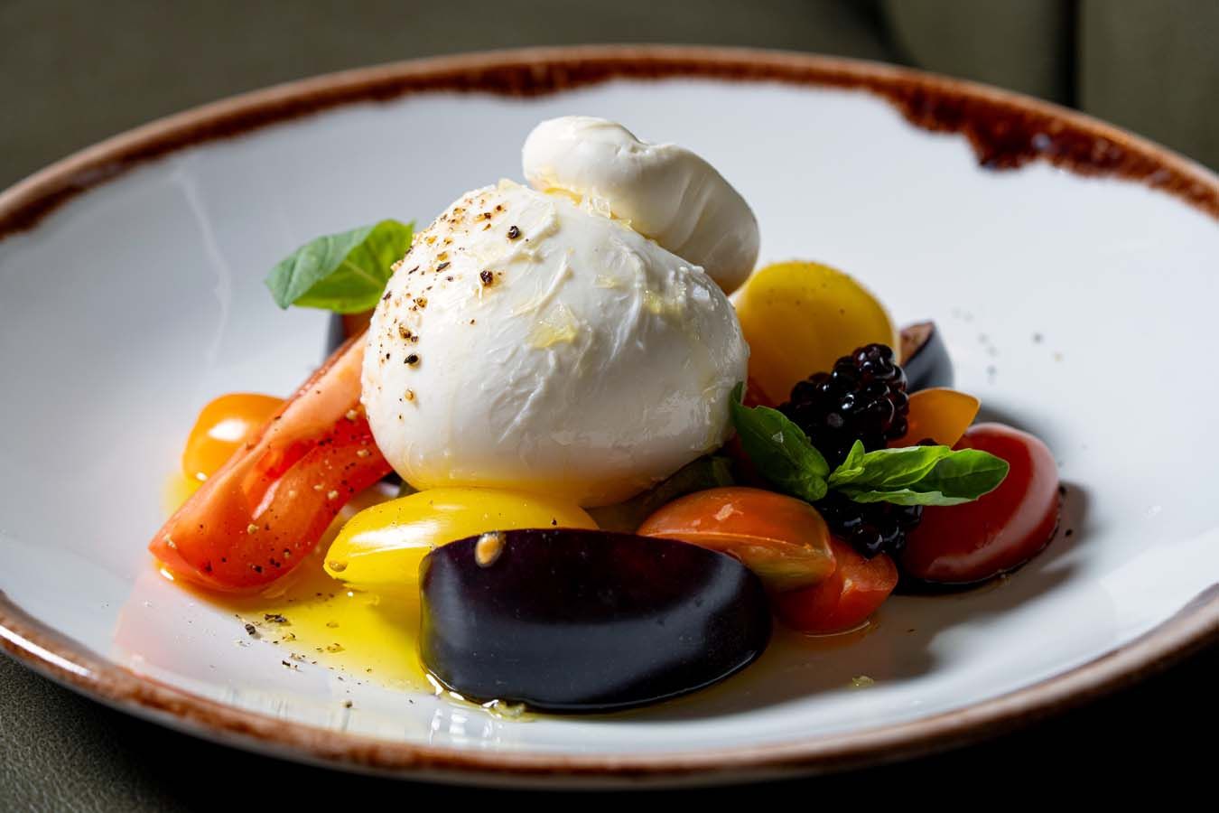 Gourmet-Dessert mit Vanilleeis, bunten Früchten und Minze auf einem weißen Teller