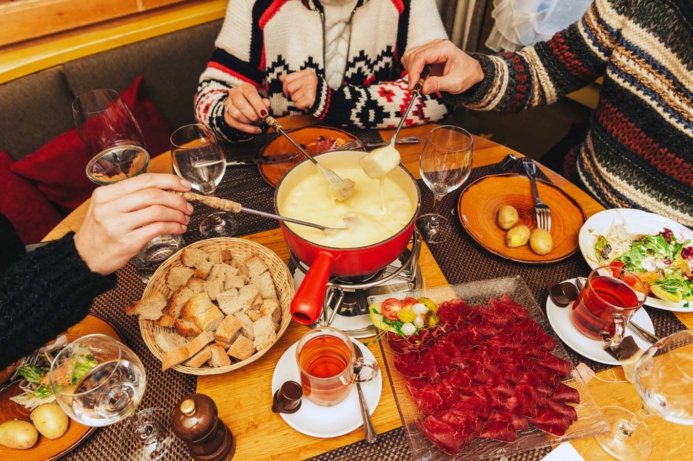 Menschen teilen sich eine Fondue-Mahlzeit an einem Tisch mit Brot, Obst und Getränken.