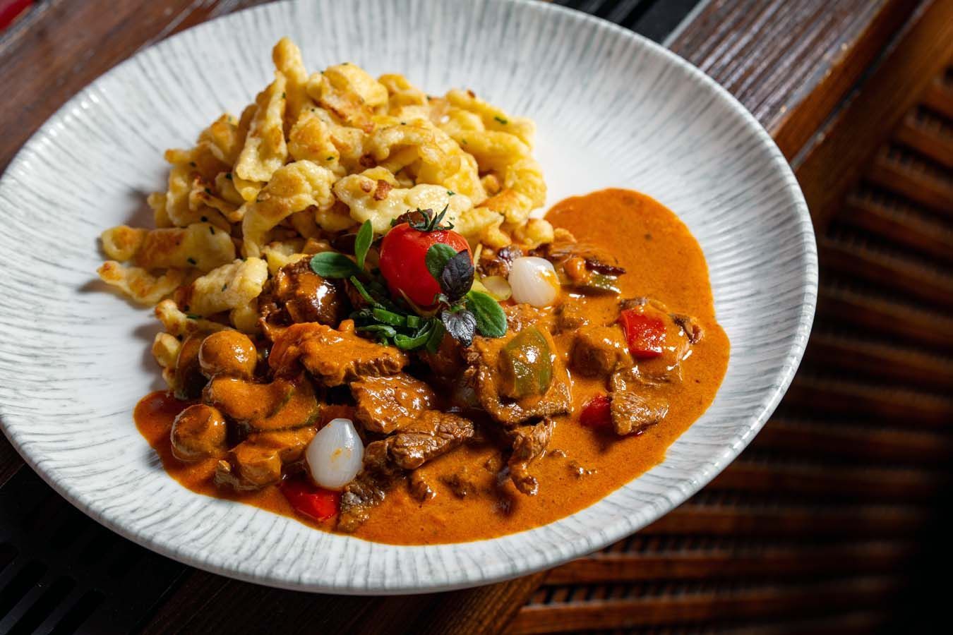 Rotes Curry mit Rindfleisch und Gemüse, serviert mit Reis und Kirschtomaten auf einem weißen Teller