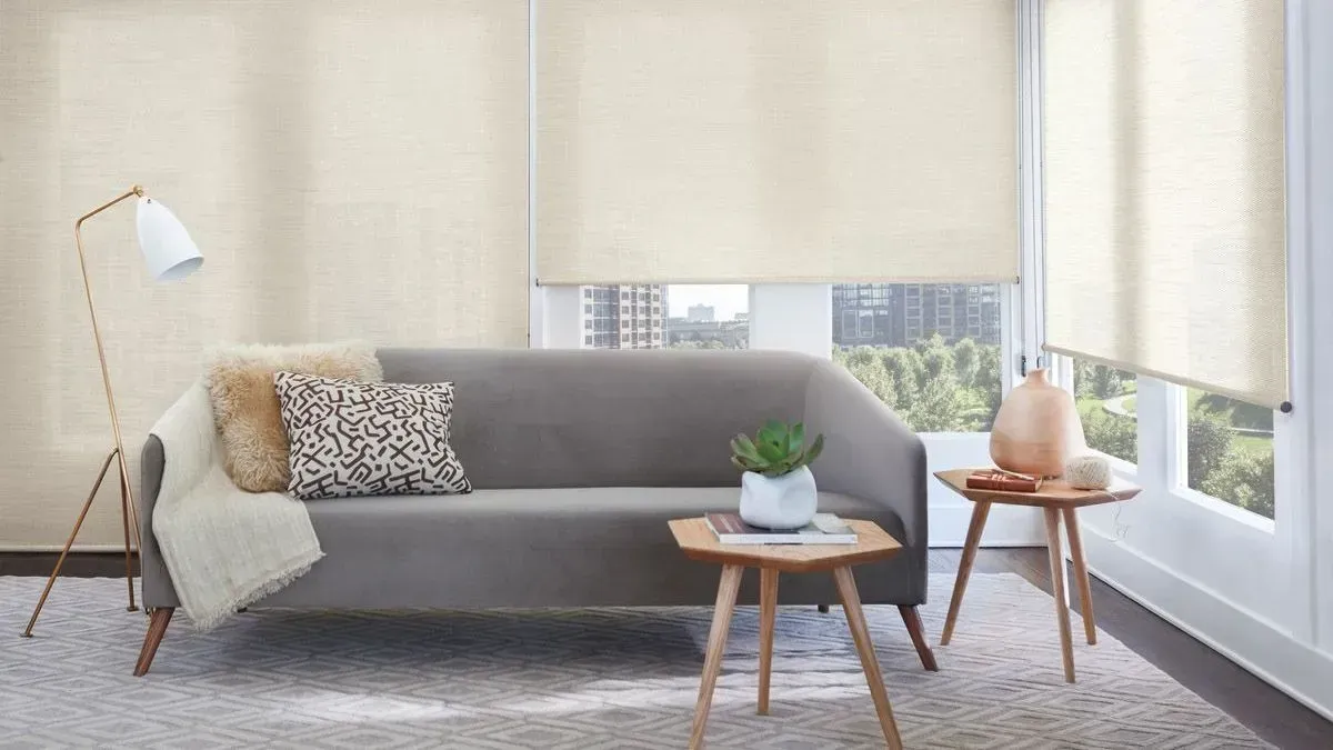 Bright living room with gray sofa, floor lamp, side tables, and large windows with blinds