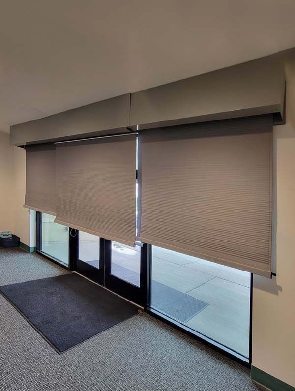 Closed beige window shades covering glass doors in a hallway lobby.