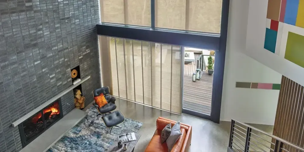 Modern living room with a fireplace, gray sofa, orange chairs, and tall windows overlooking a patio