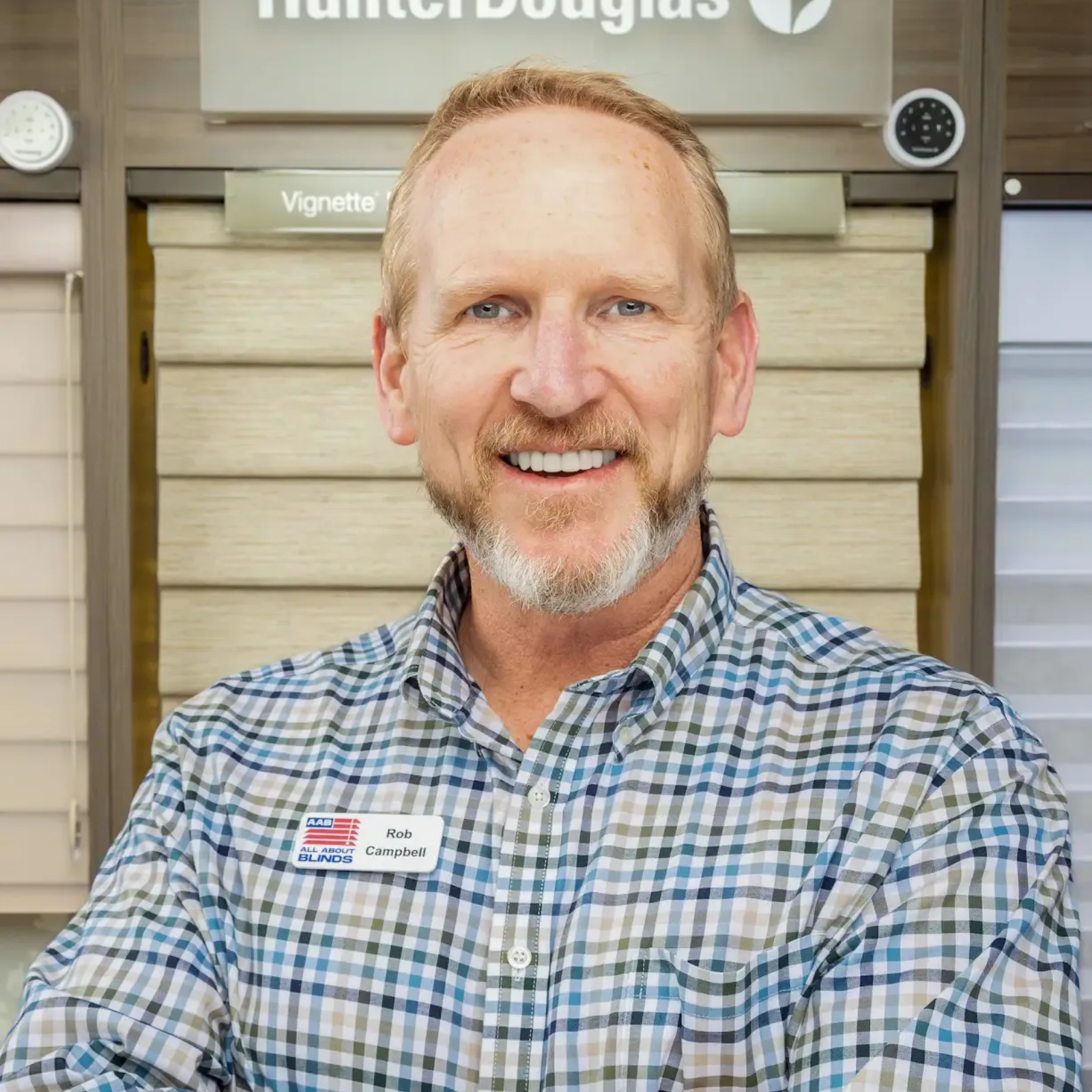 Smiling man in a plaid shirt standing in a Hunter Douglas showroom display area