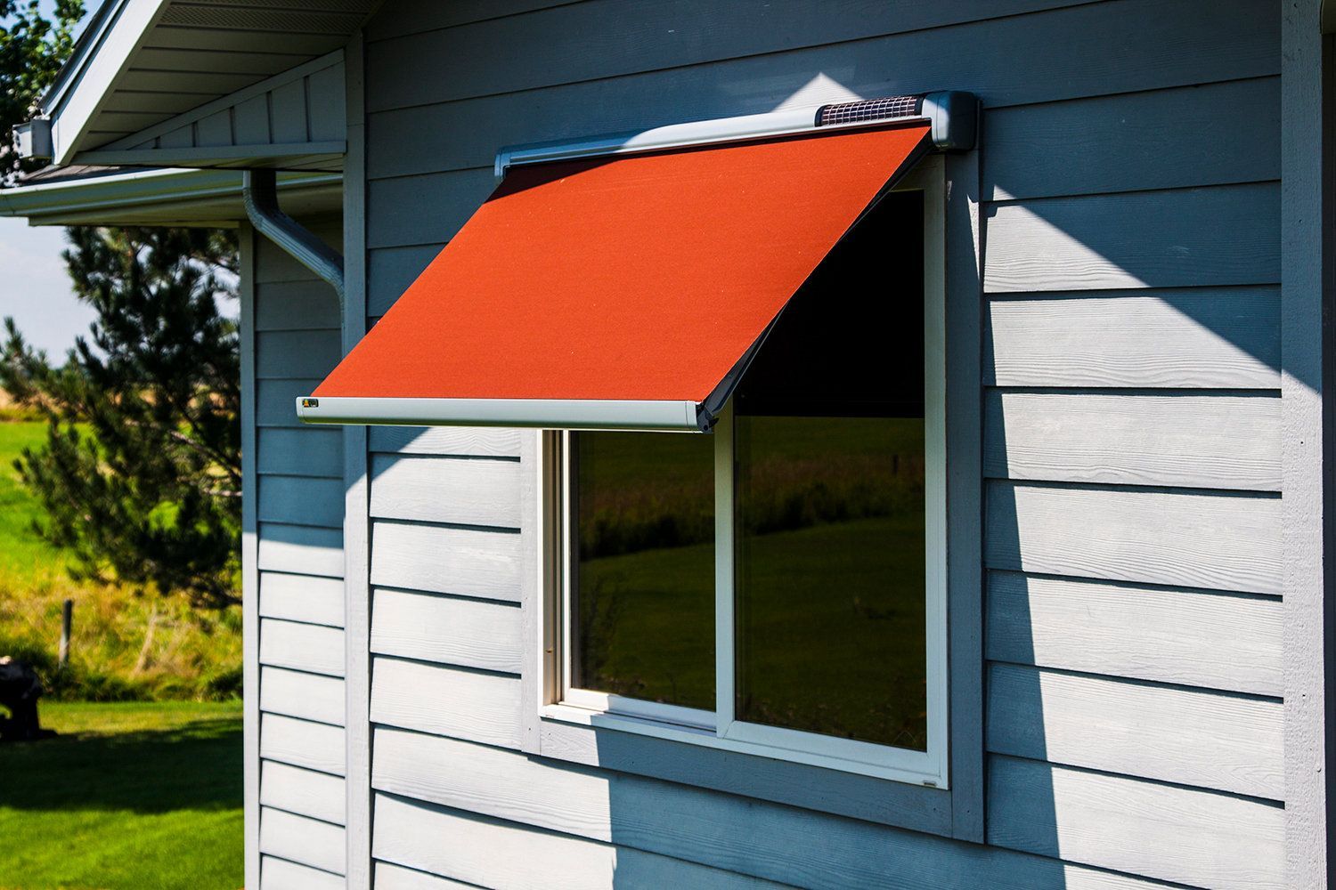 Red awning over a window on a gray house exterior.