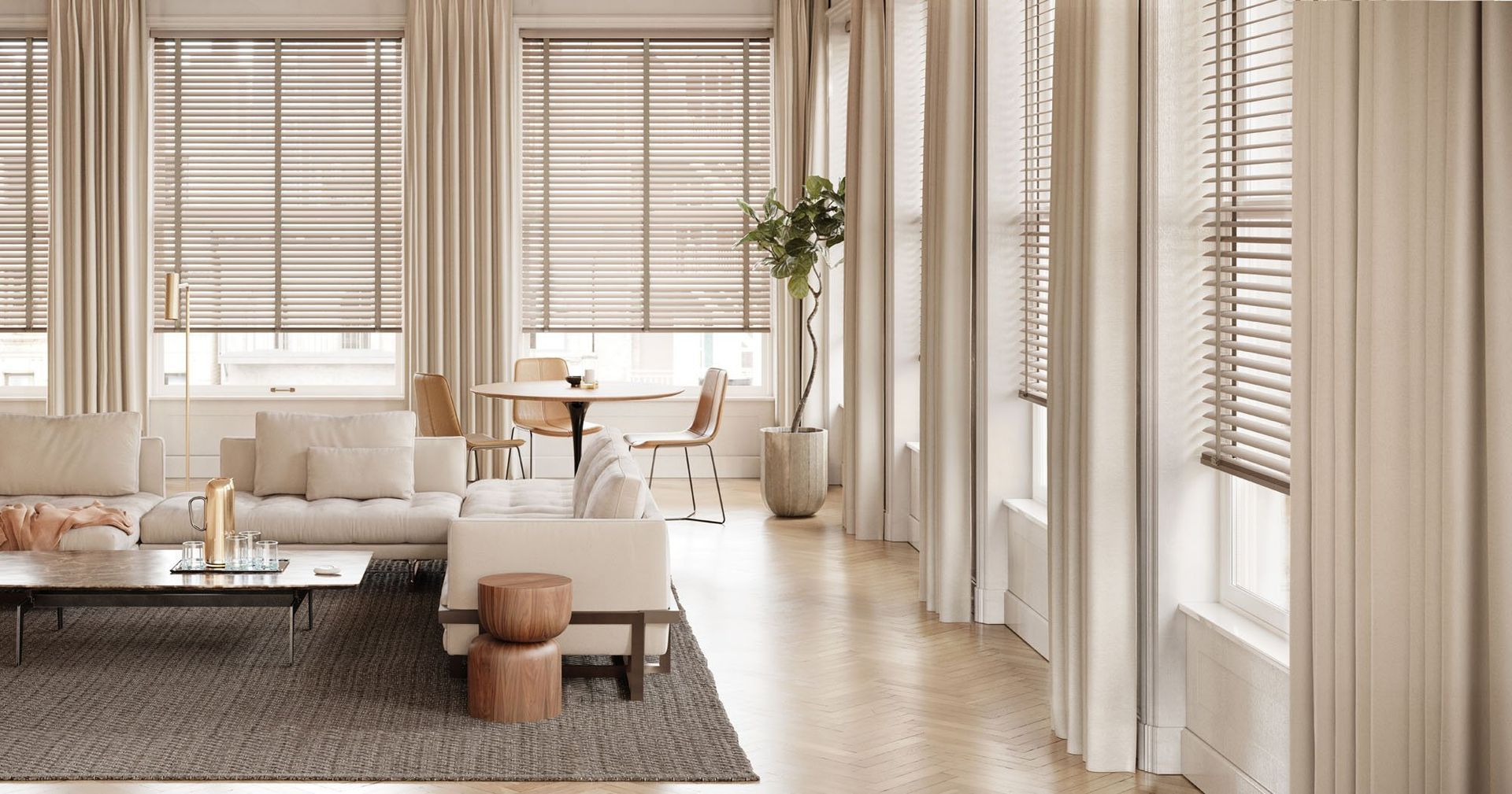 Bright beige living room with large windows, blinds, sofa, coffee table, and a dining nook with plants.