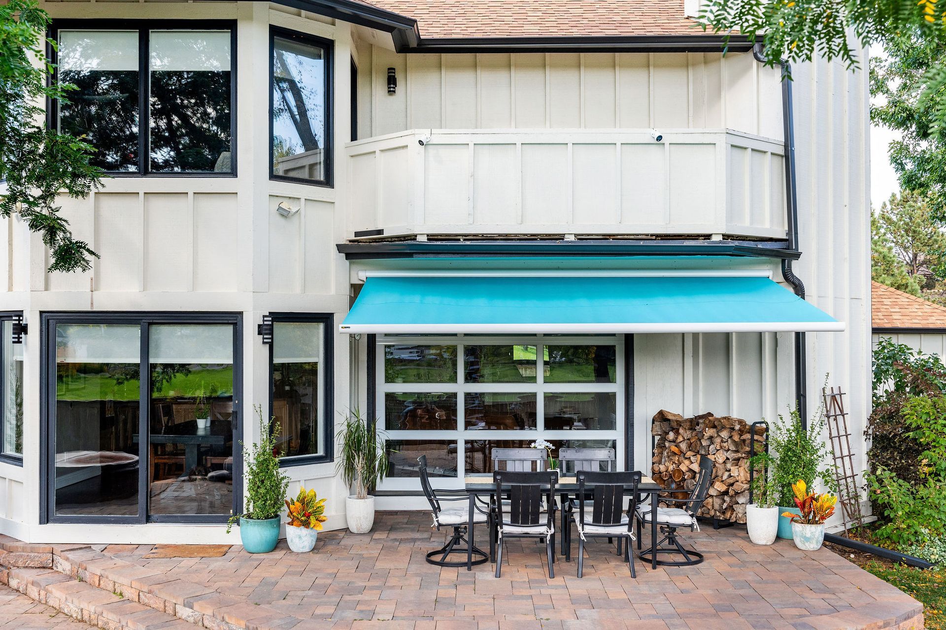Modern two-story house exterior with patio, turquoise awning, glass doors, and outdoor dining set