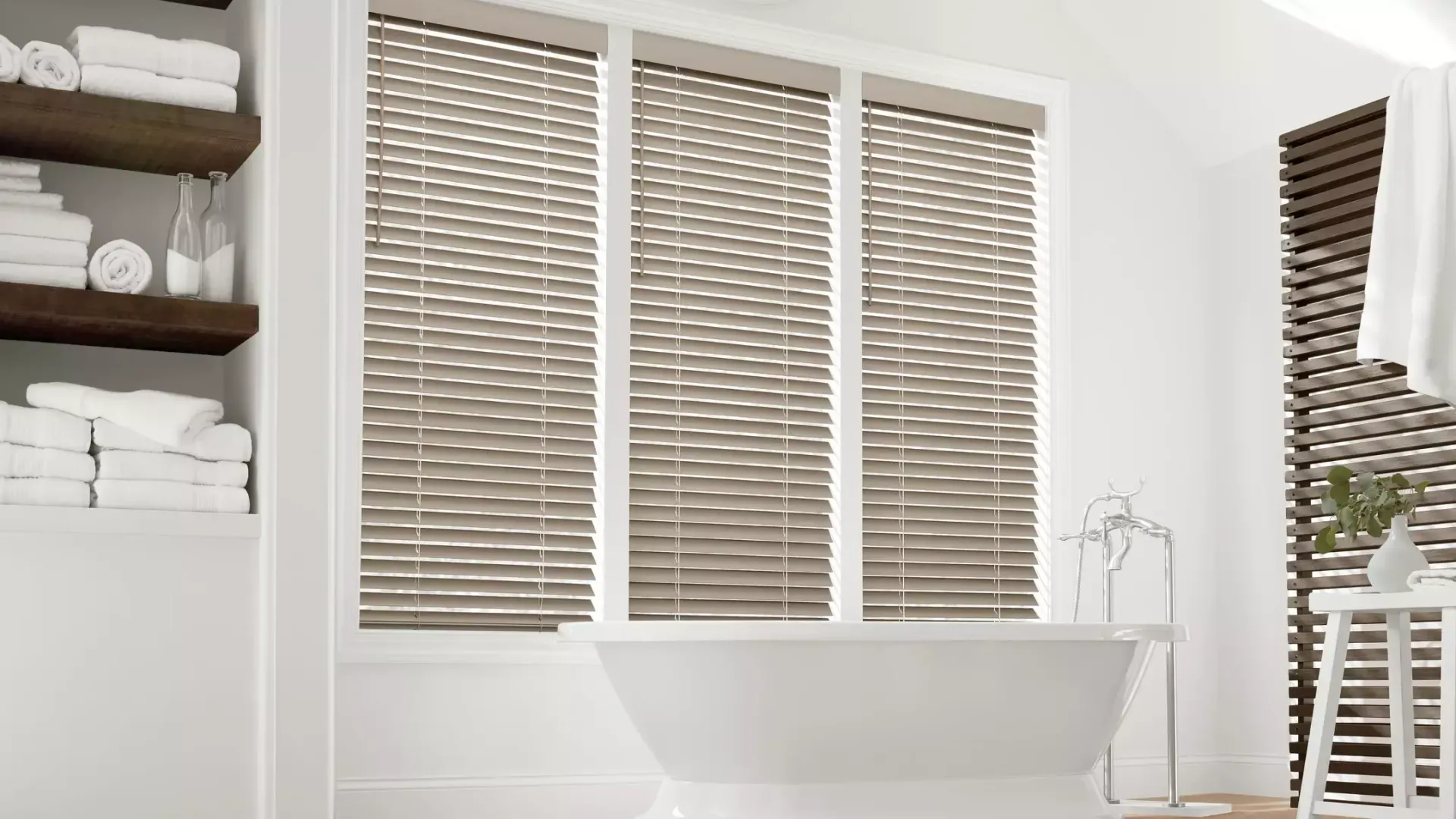 Bright bathroom with white tub, woven window blinds, towel shelves, and a potted plant