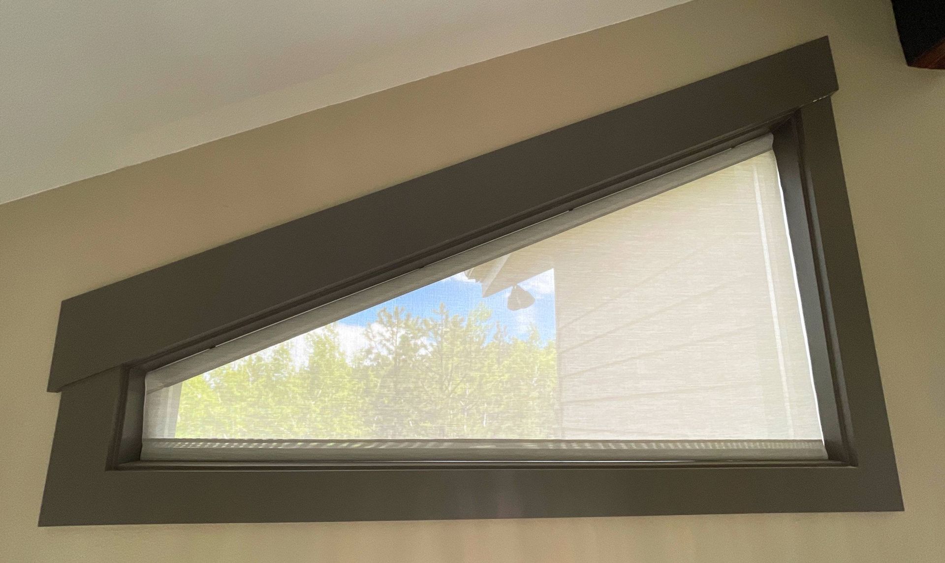 Insolroll® Solar Shades and Sun Shades on an angled window, overlooking a blue sky and trees