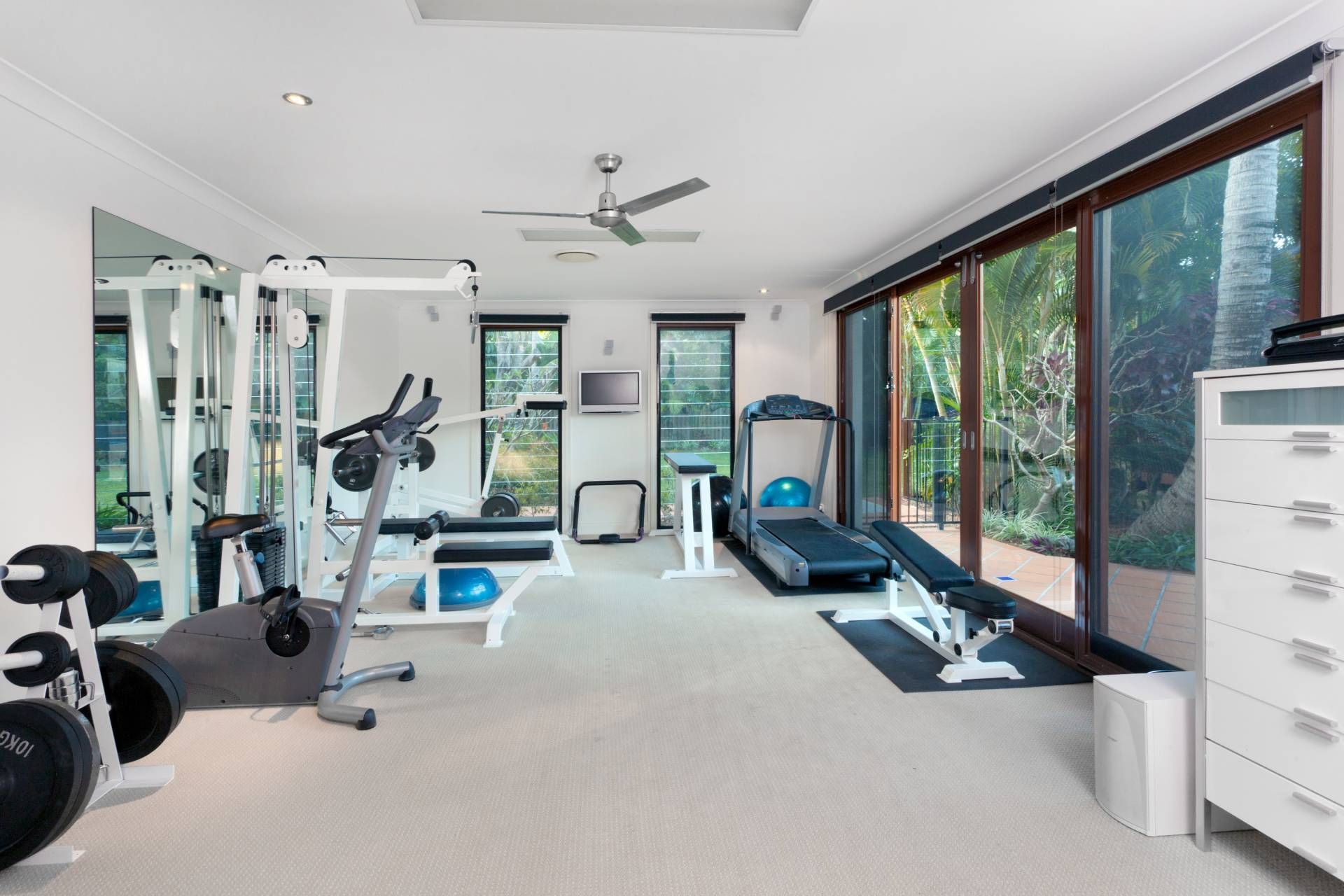 An organized home gym with large windows and a sliding door in need of durable blinds