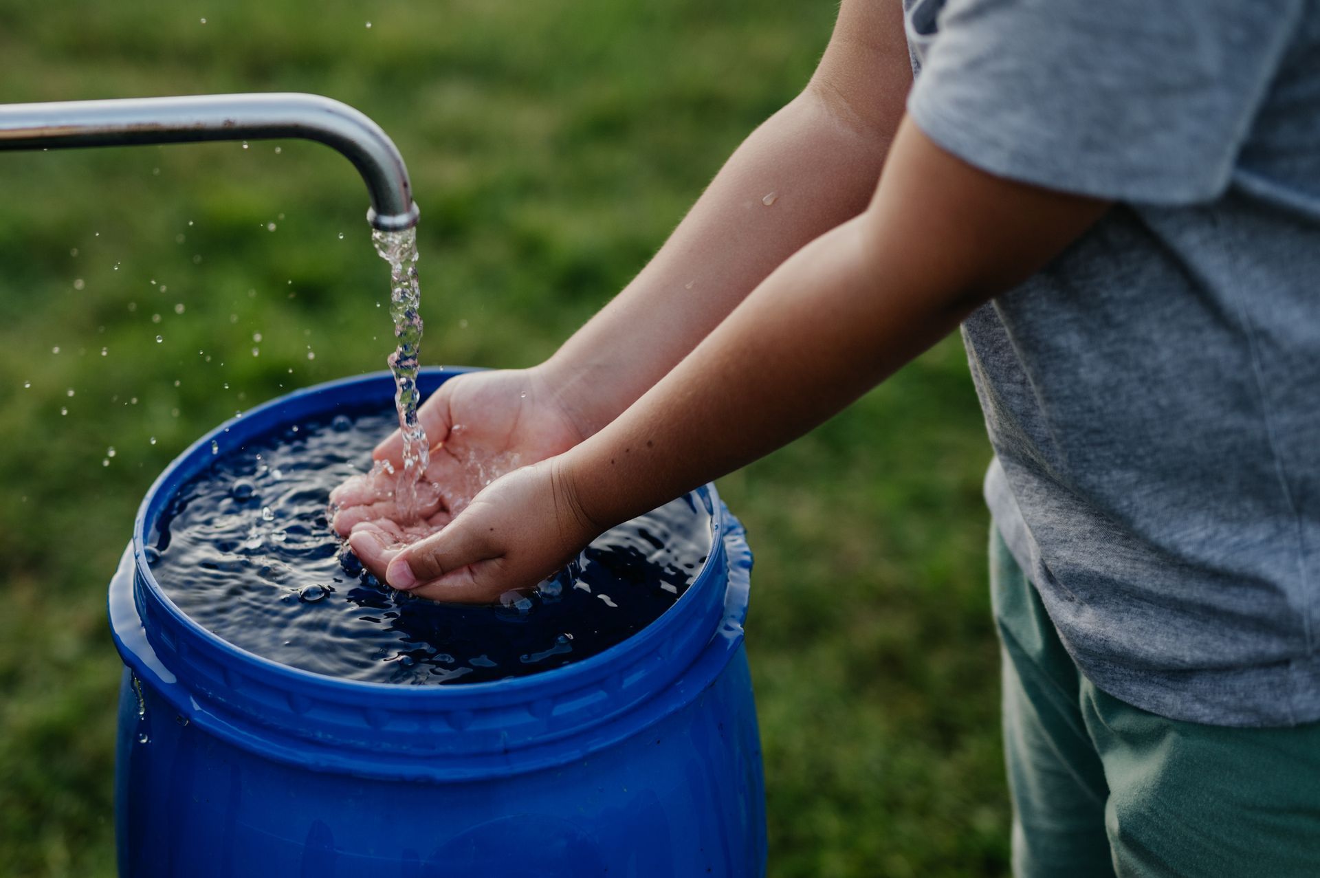 A close-up of a boy washing his hands with water from a well.