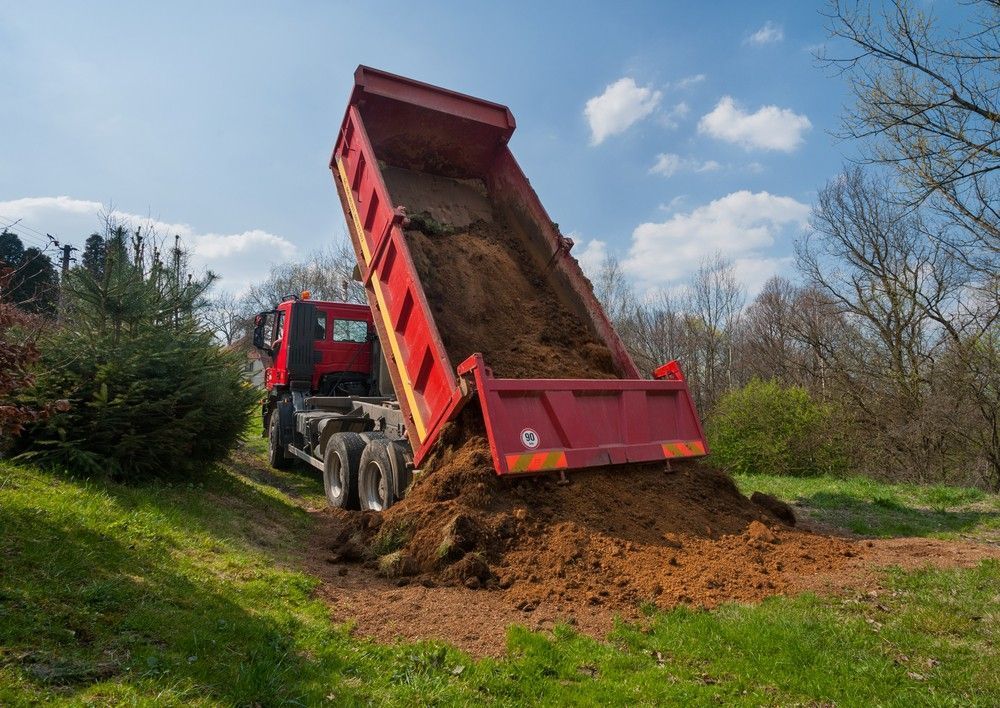 Red Dump Truck Unloading Dirt on A Grassy Slope — Macca's Dynamic Earthworks in Tolga, QLD