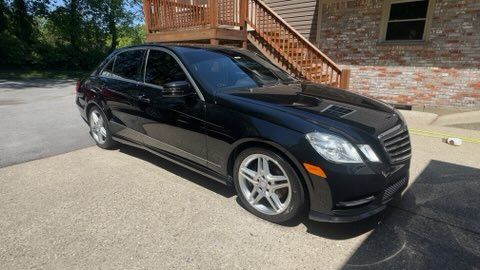 Black sedan parked on a driveway beside a brick building with wooden steps.