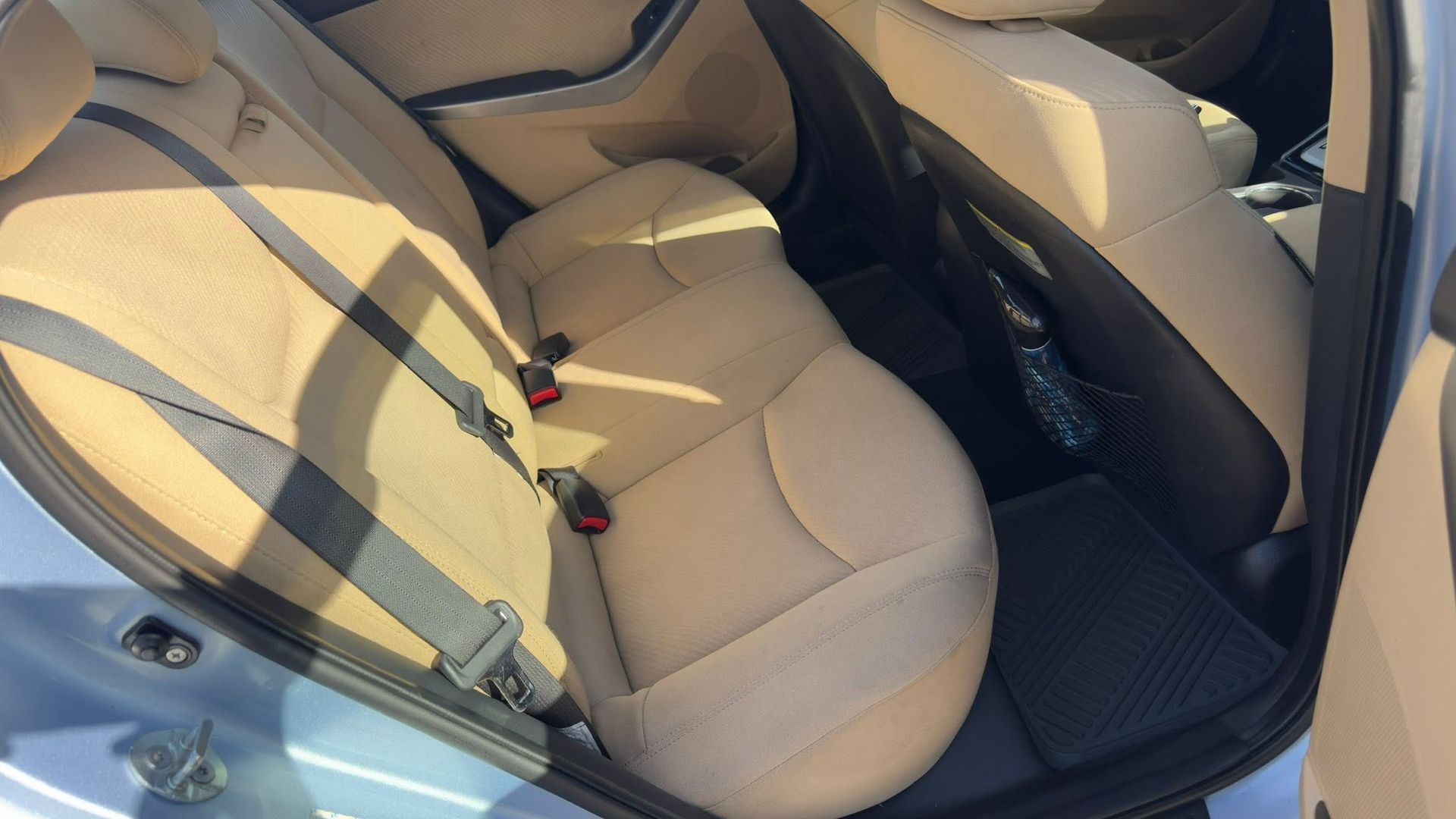 Tan car seats inside a car, with seatbelts fastened across the back seat.