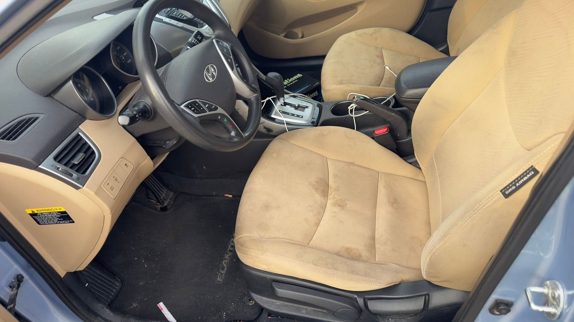 Tan interior of a car with beige seats and steering wheel, viewed from the open driver’s door