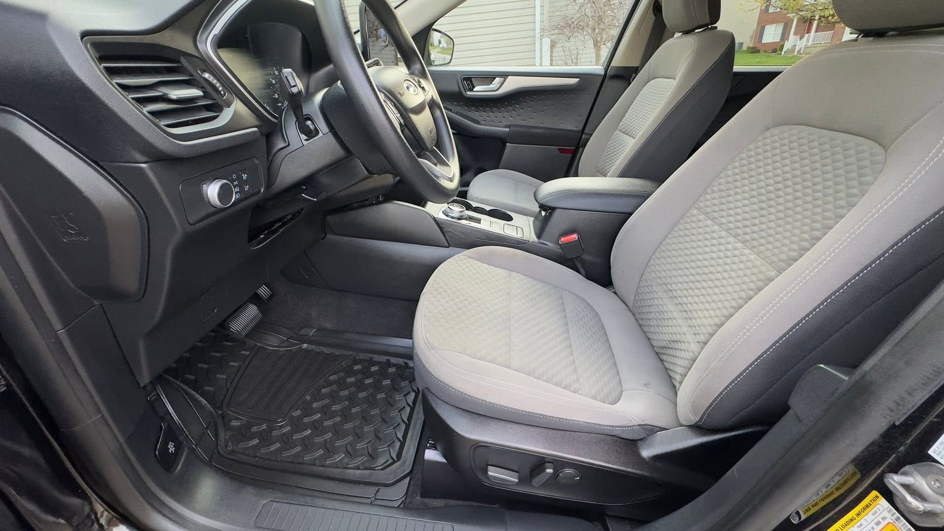 Car interior with gray front seats, black dashboard, steering wheel, and floor mats.