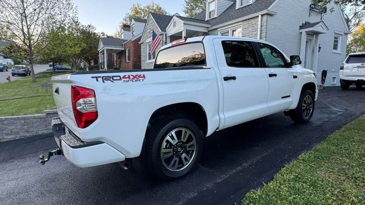 White pickup truck parked in a suburban driveway beside a house, rear-side view.
