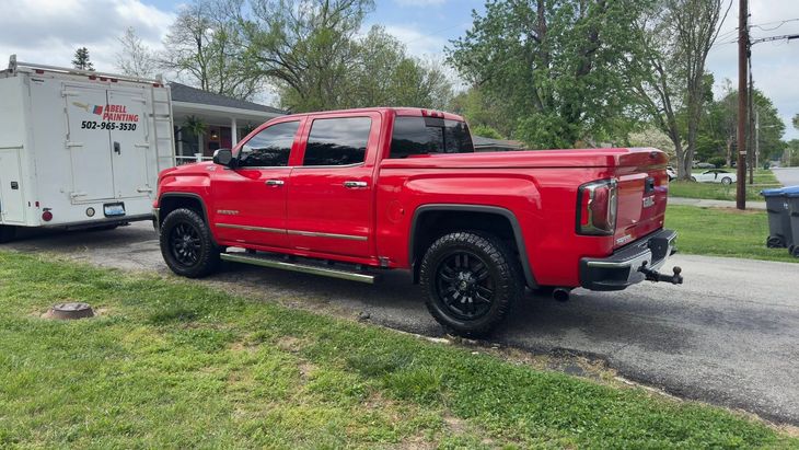Red pickup truck parked on gravel beside a white trailer in a grassy yard