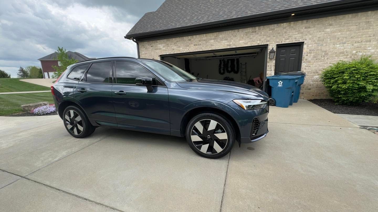 Dark gray SUV parked in a driveway beside a garage with blue recycling bins