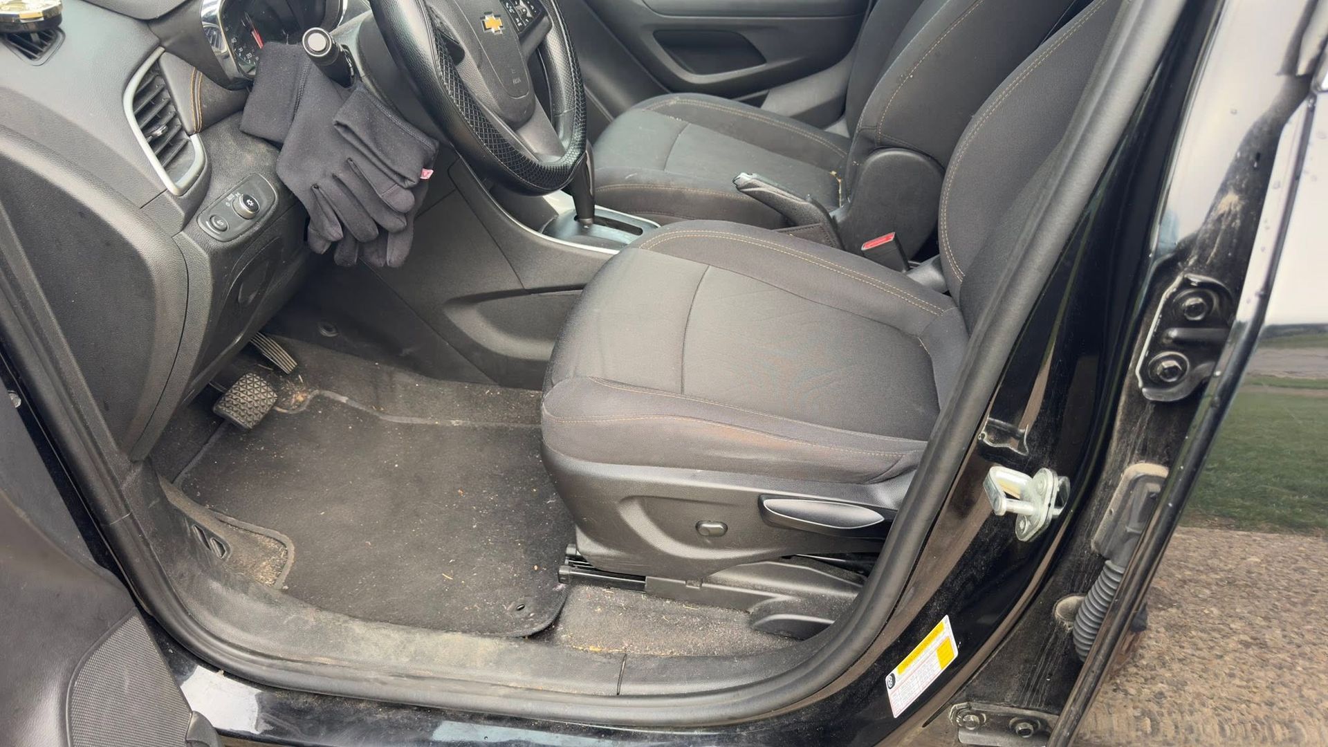 Car interior with black seats and open rear door, showing dirty floor mats and a jacket on the seat