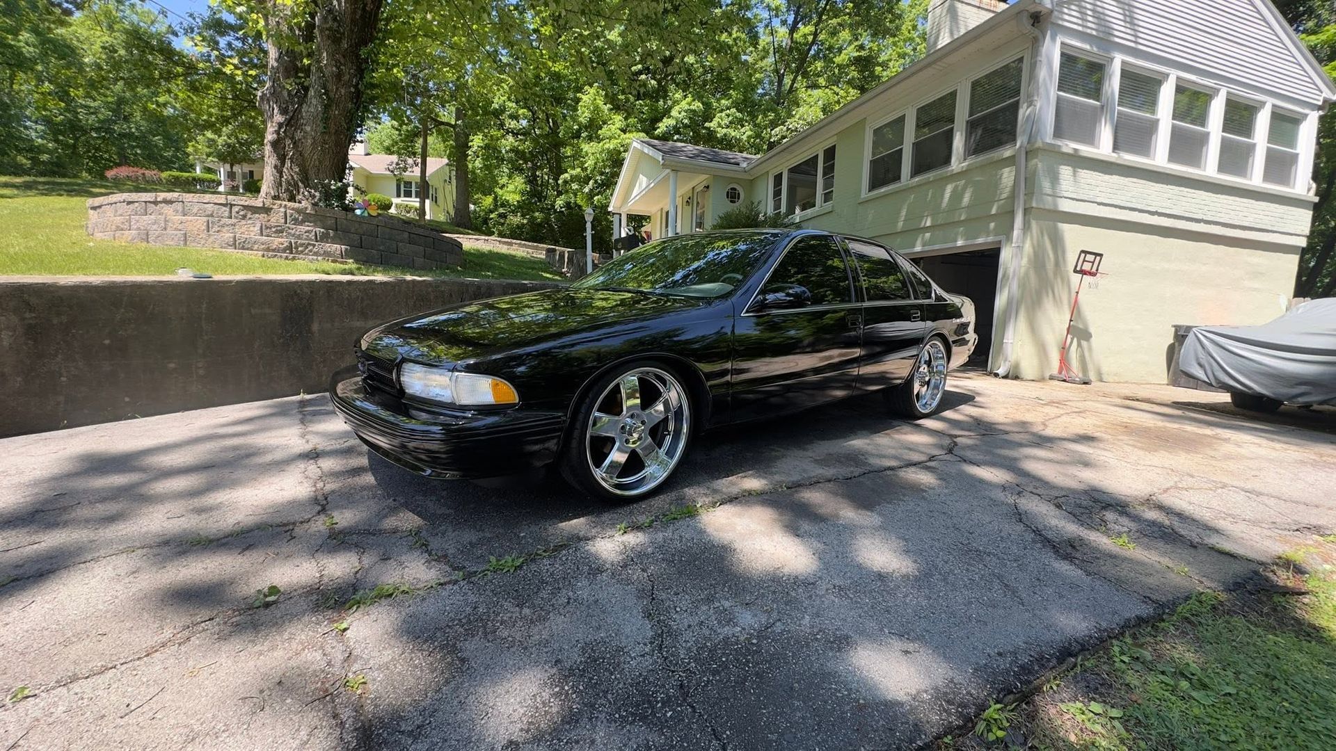 Black sports car parked in a driveway beside a beige garage with trees in the background