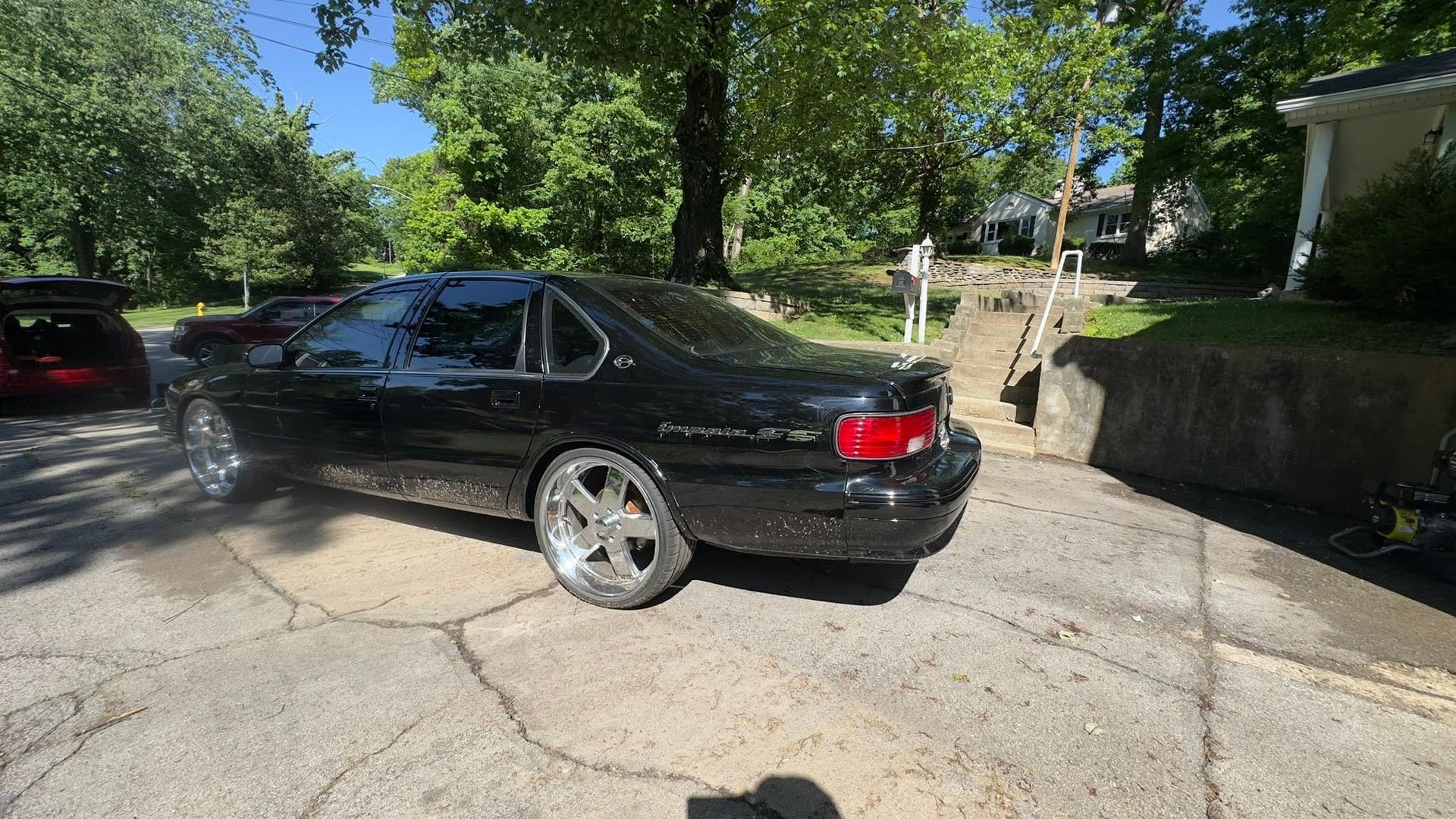 Black sedan parked on a sunlit driveway beside a stone wall and trees