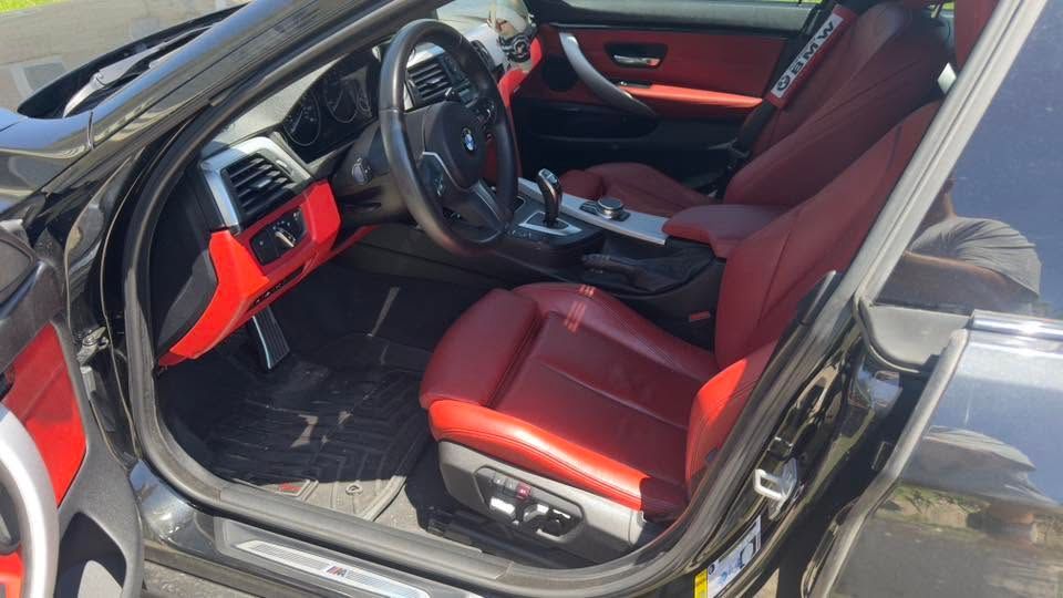 Black car interior with red leather seats, dashboard, and steering wheel visible through open driver door