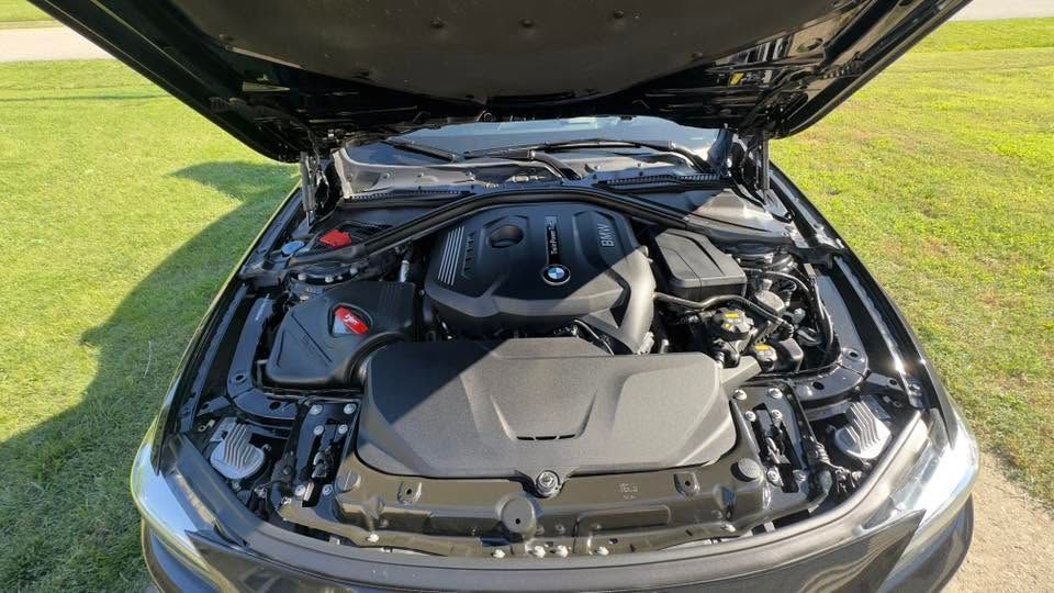 Open car hood showing a clean engine bay in a silver vehicle on grass.