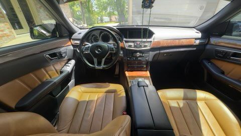 Luxury car interior with tan leather seats, black dashboard, and steering wheel viewed from the back seat