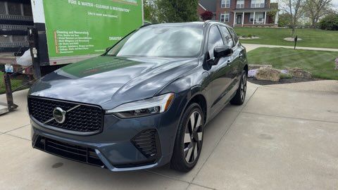 Dark blue Volvo SUV parked on a driveway beside a green sign and grassy lawn.