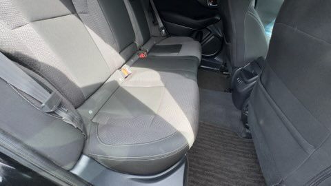 Car back seat with gray upholstery and black floor mats in sunlight