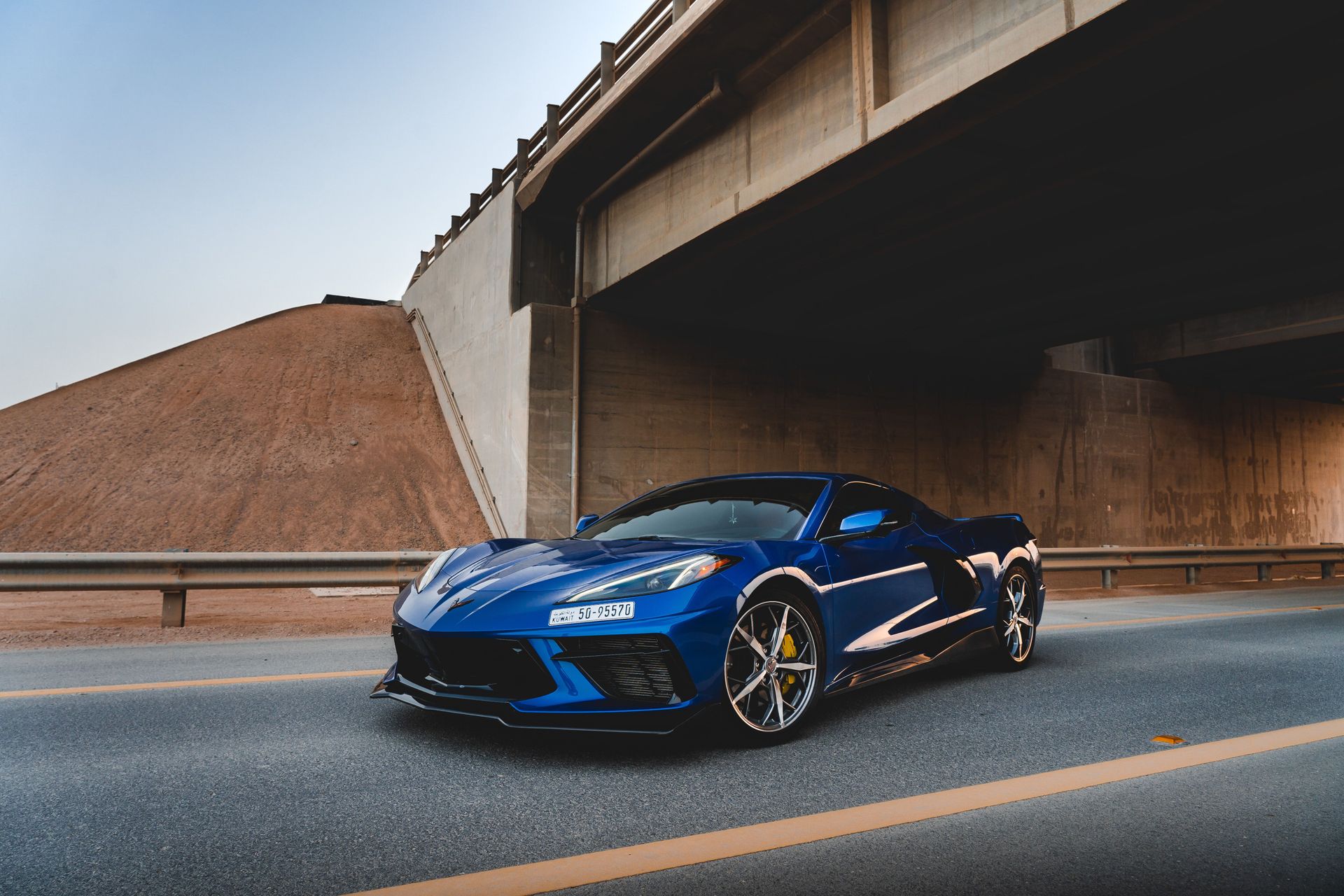 Blue sports car parked on a road beneath a concrete overpass at dusk